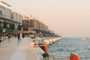 A serene view of Istanbul's waterfront promenade with people walking and boats on the water at dusk.