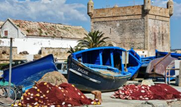 Colorful fishing boats and nets by the historic fort in Essaouira, Morocco, under a clear blue sky.