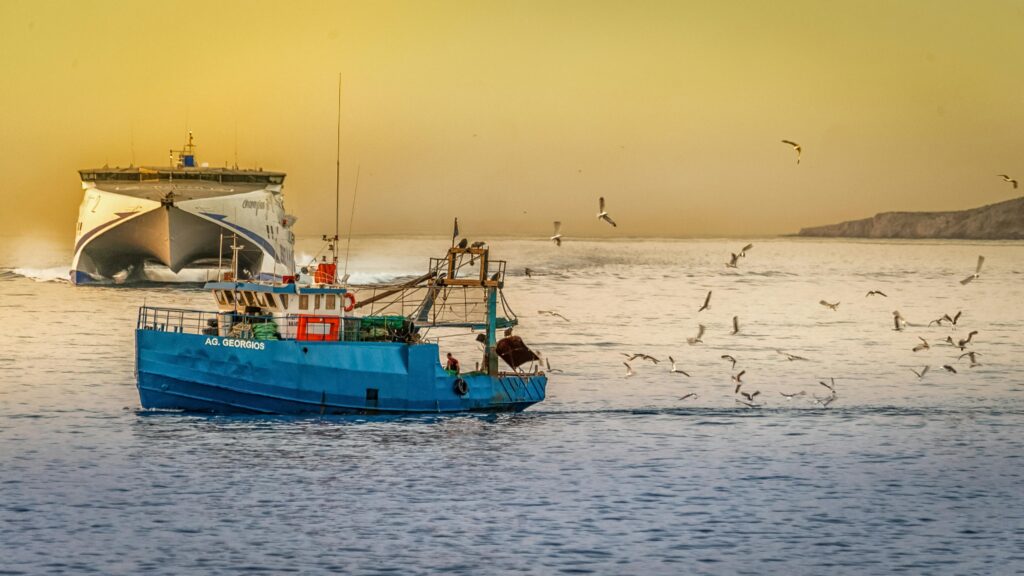 Fishing boats and seagulls in Rethymno, Greece at sunset with a ferry in the background.