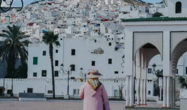 A woman in traditional attire in Tetouan, Morocco, with hillside architecture in the background.