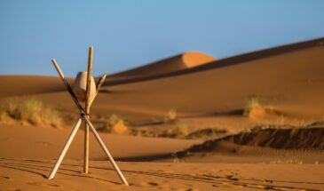 Peaceful desert landscape at Merzouga with sand dunes and wooden tripod under clear blue sky.